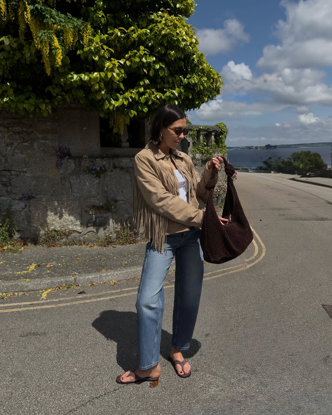 woman wearing loose jeans, suede fringe jacket, and suede flip flops