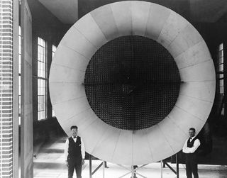 Two mechanics pose near the entrance of Langley's first wind tunnel.