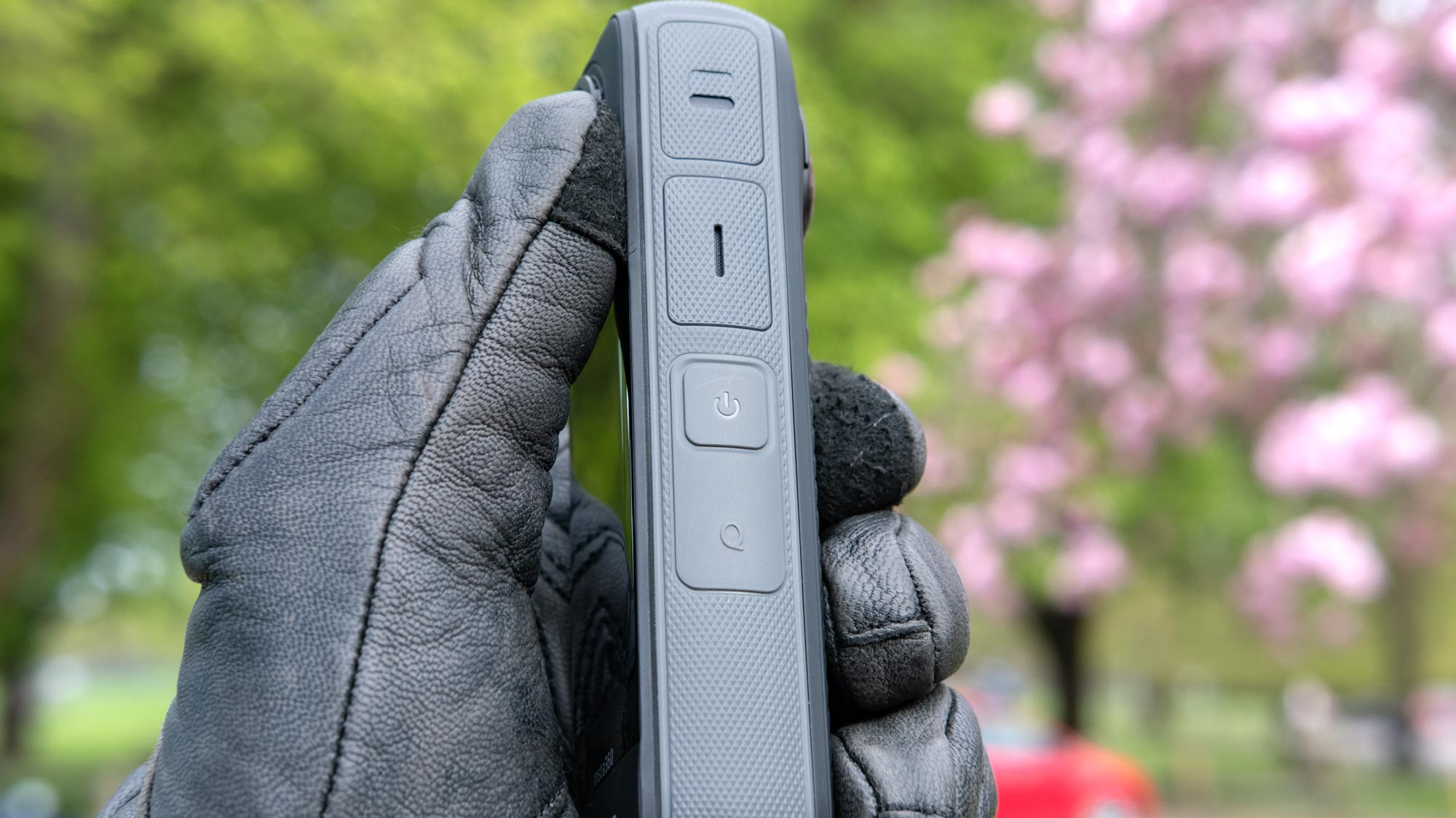 A photo of the Insta360 X4 being held in a leather gloved hand with the side Q and power buttons showing.