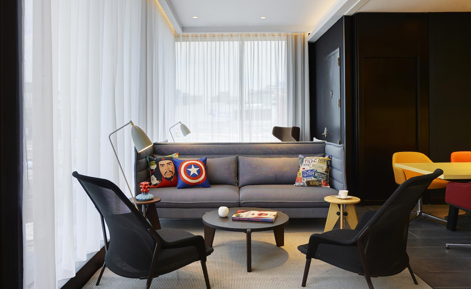 CitizenM North Gate lounge with grey sofa, two black armchairs, yellow dining table with orange chairs and dark wooden panels