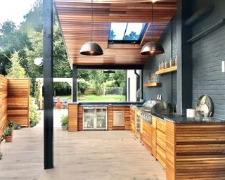 An L-shaped wooden clad outdoor kitchen with wooden floor and wooden clad roof