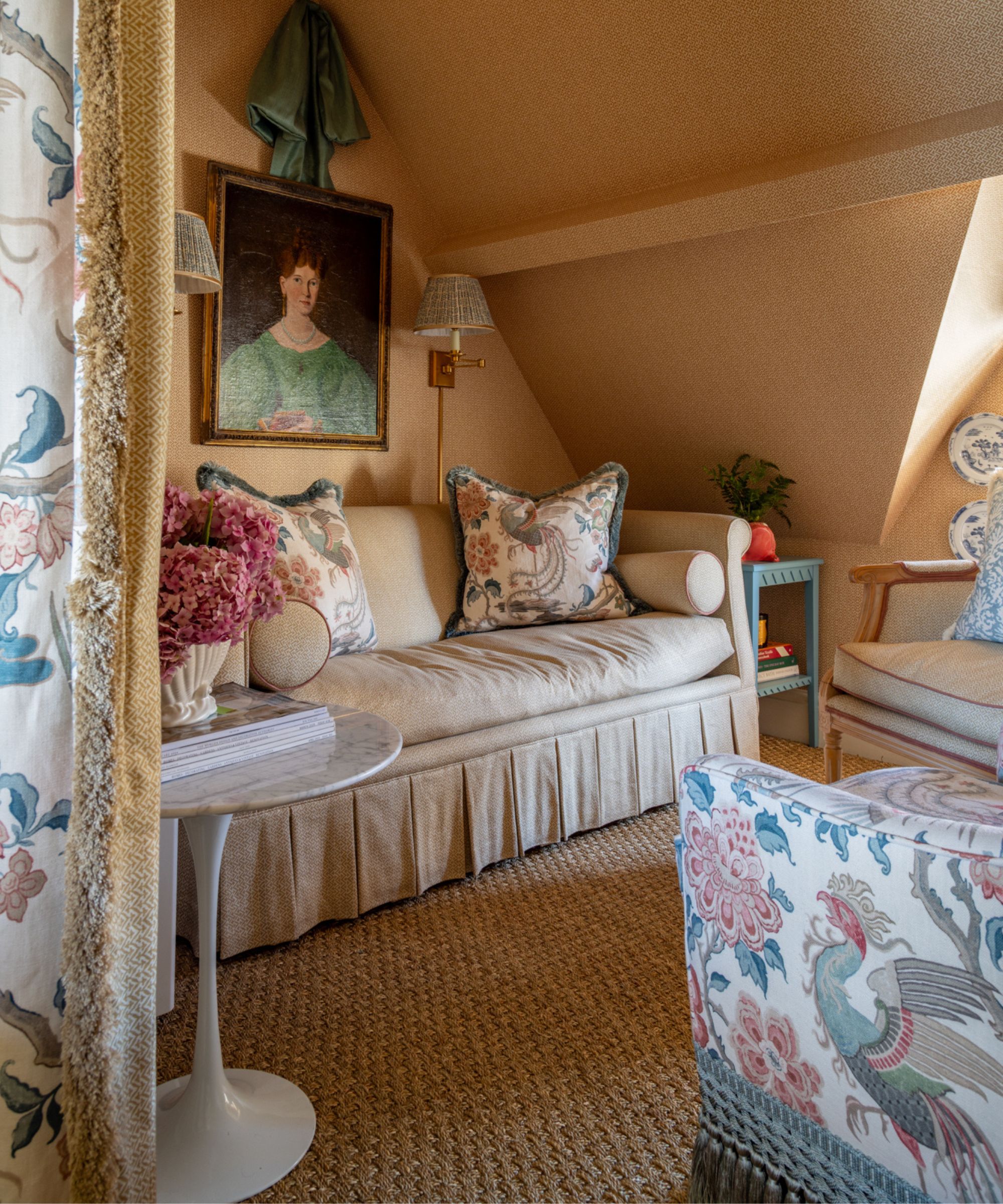 warm yellow wallpapered seating nook with a skirted couch styled with fringe trim patterned pillows sat opposite a floral arm chair with tassel trim