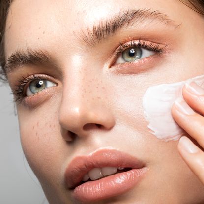 Young woman applying skincare to her face with bright glowy skin