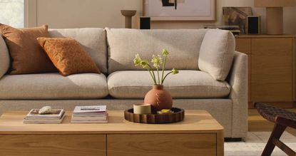 A modern, cream sofa with orange cushions, alongside a wooden coffee table, all from AllModern.