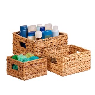 Three light brown woven baskets in varying heights, with the largest one with blue bottles in it and the smallest one with green and blue loofahs in it