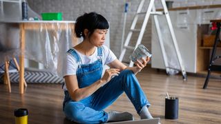 woman sat on floor in home renovation looking at tin of paint