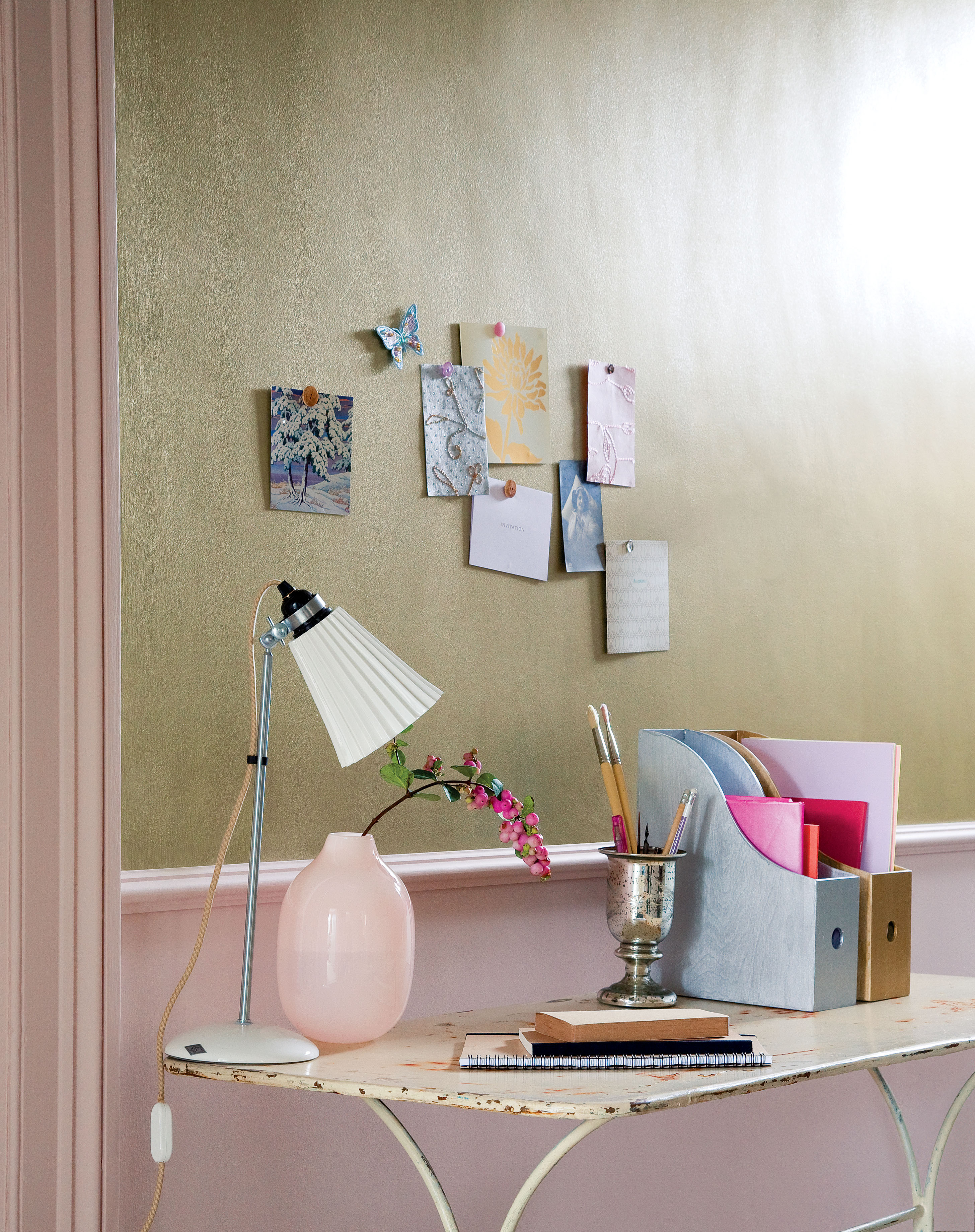 a vintage side table with a vase, folders and a lamp on, in front of a pink and green wall