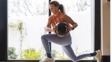 woman performing a lunge and rotation move holding a medicine ball weight in front of a large window 