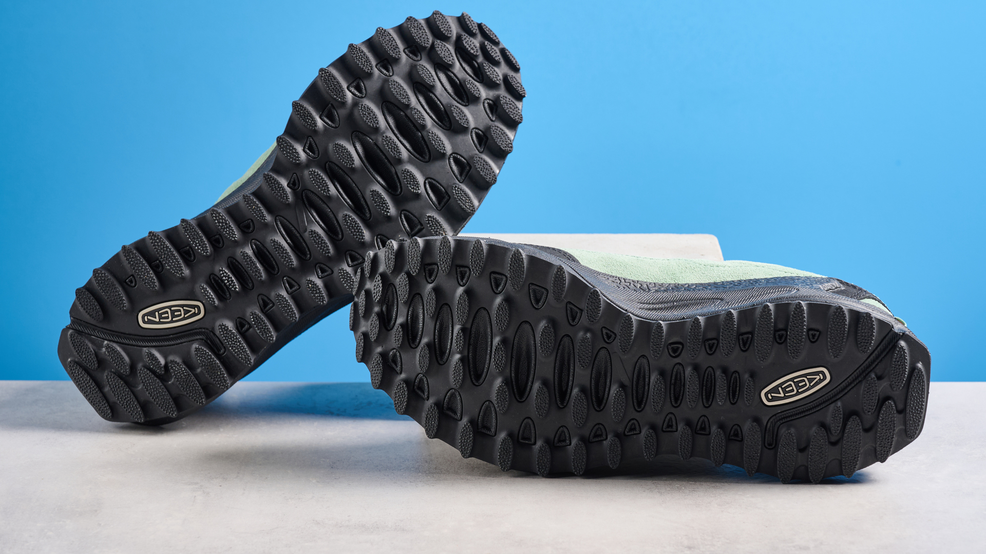 The Keen Jasper Zionic hiking shoes in green/gold colorway are photographed against a blue Tom&#039;s Guide background and a stone floor, showing the lug sole and the leather upper with orange laces