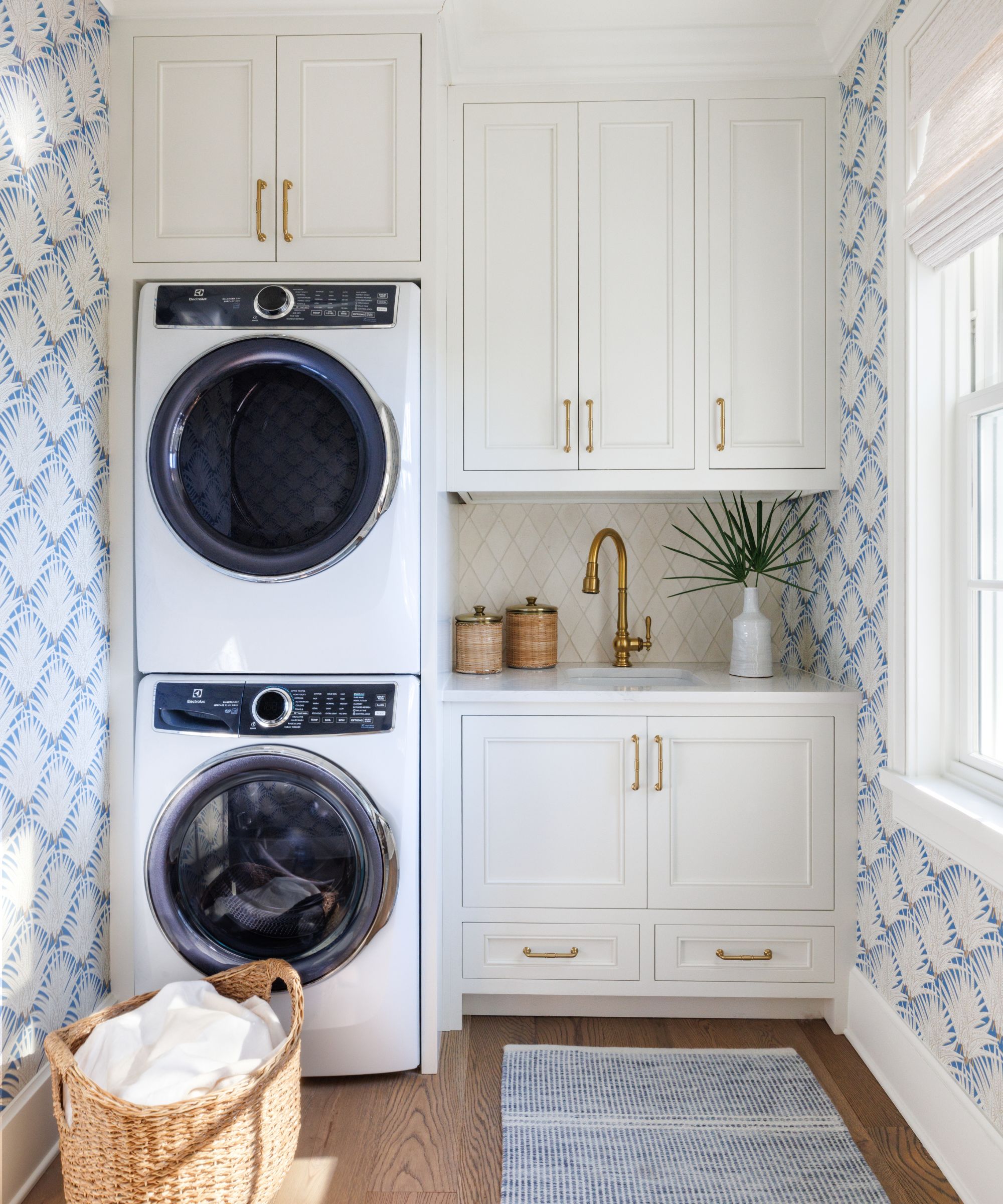 Small laundry room with stacked appliances, white fitted cabinets and wallpaper