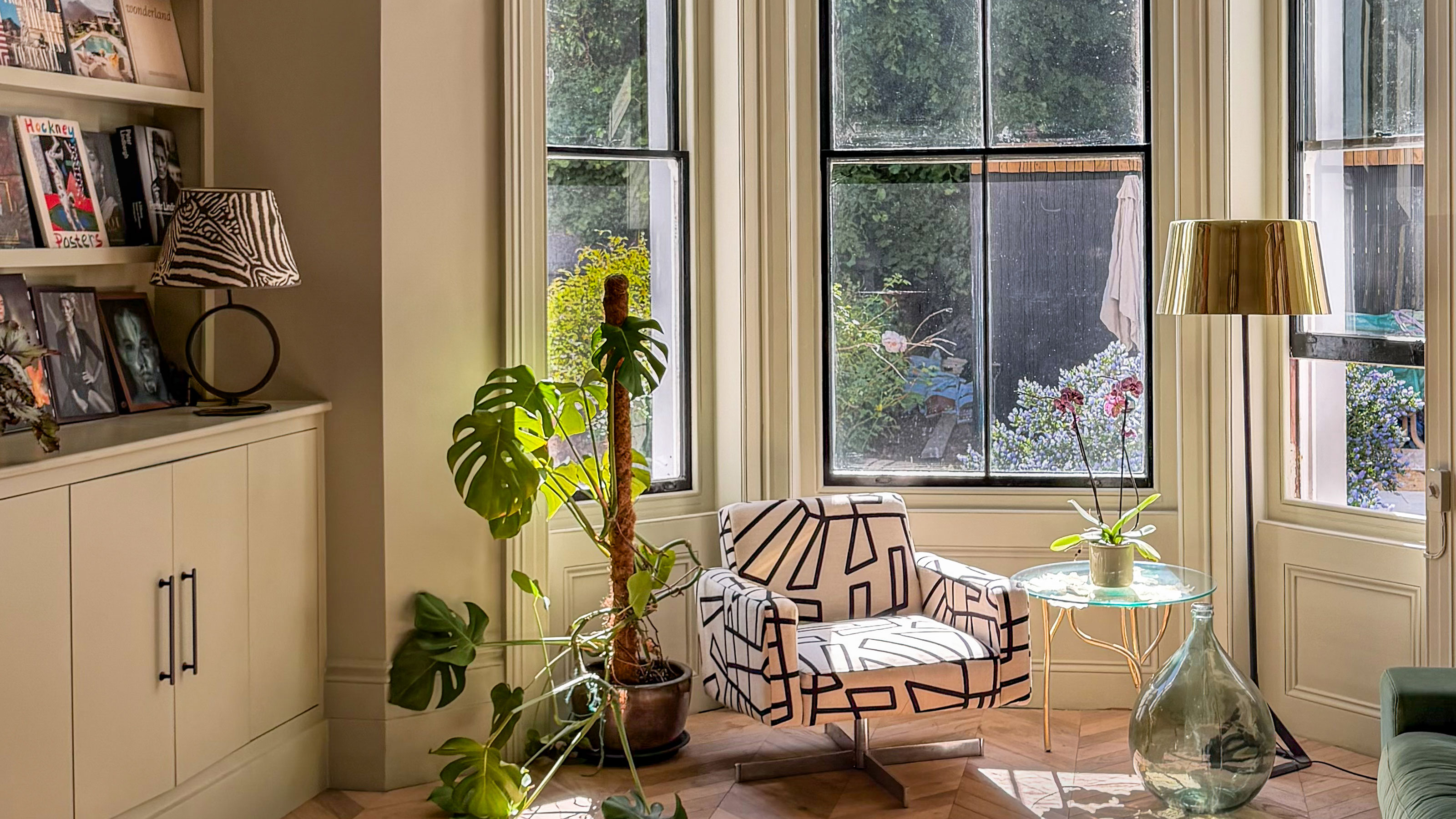 Bay window with floor lamp, armchair covered in abstract pattern, glass coffee table and houseplants