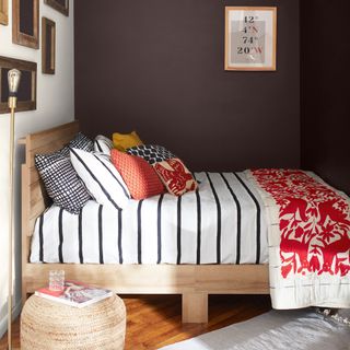 small bedroom colour ideas, small bedroom with chocolate and white walls, wooden bed, stripe bedding red throw, cushions, artwork, rattan footstool, wood floor