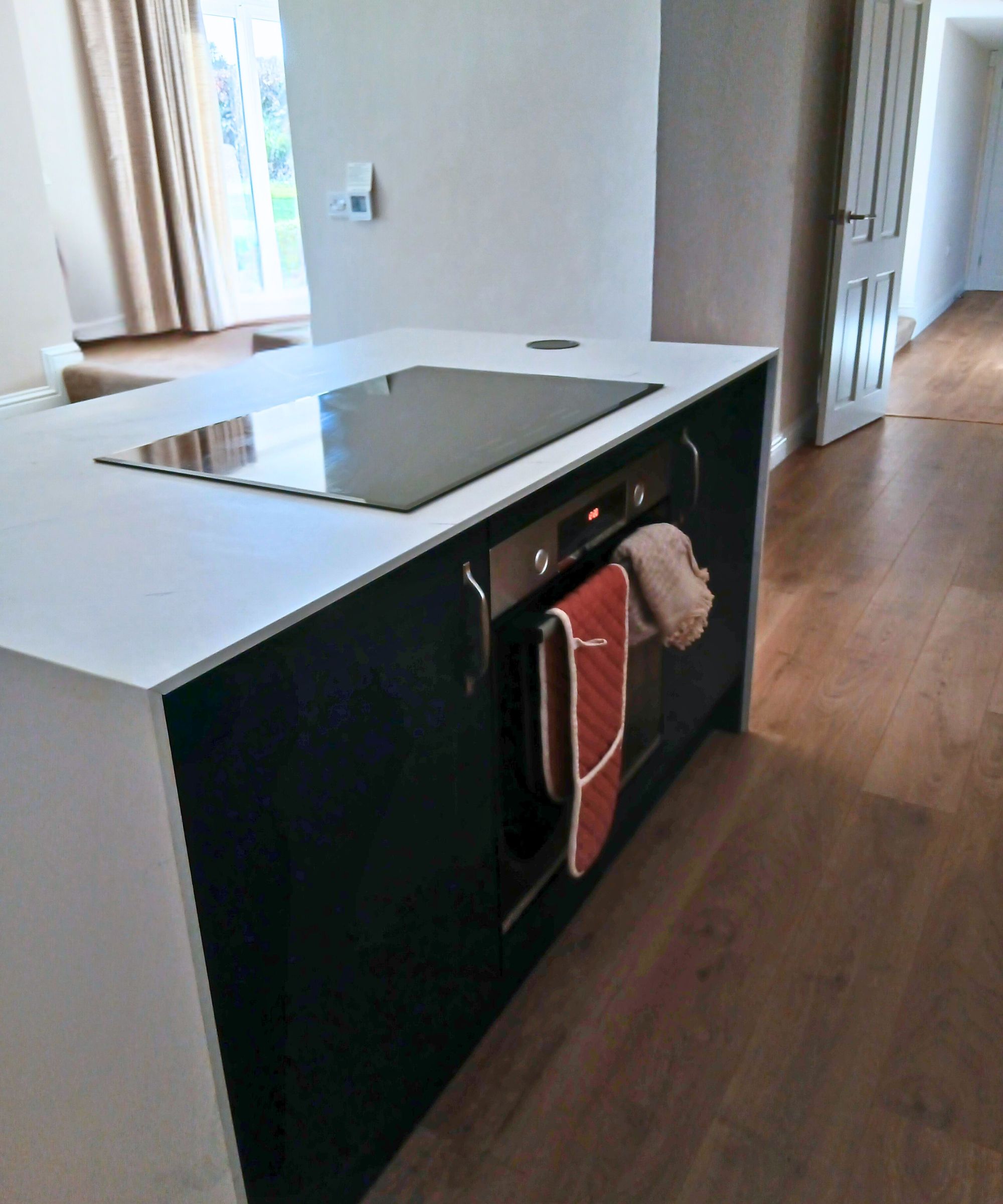 A compact kitchen island sits in the centre of the room, featuring a white waterfall-style worktop and a black induction hob.