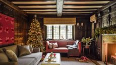 A cosy living room with two sofas, with exposed ceiling beams, a tall decorated Christmas tree and fireplace with a lit fire.