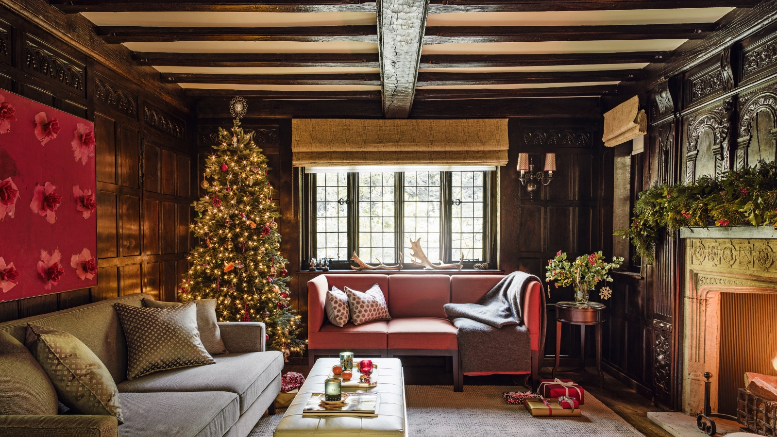 A cosy living room with two sofas, with exposed ceiling beams, a tall decorated Christmas tree and fireplace with a lit fire.