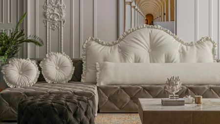White WOWMAX ruffle headboard pillow styled atop a velvet grey button-tufted couch inside of a white living room featuring ornate molding and classical artwork