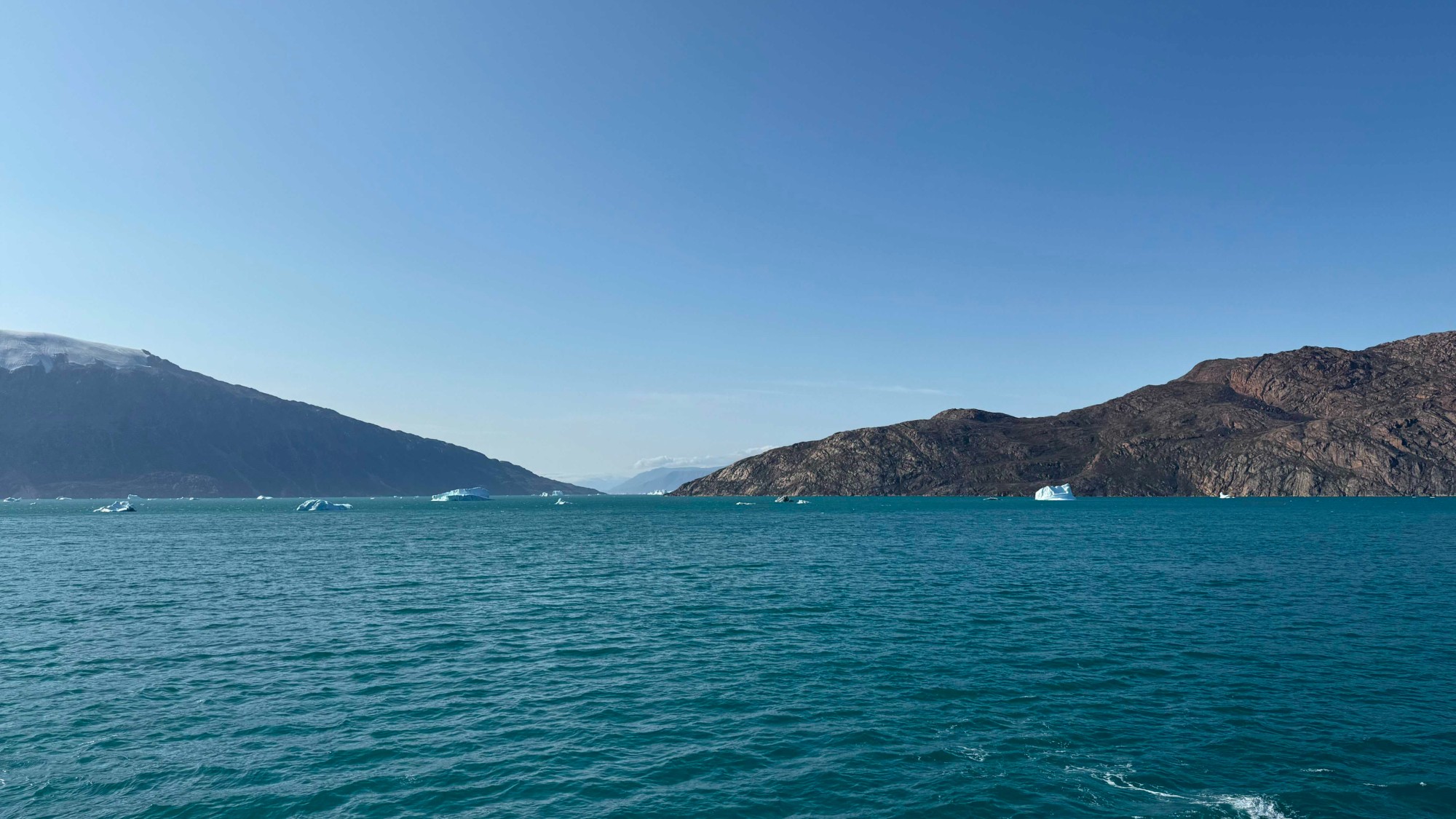mountain peaks line the blue waters of a bay under a clear sky