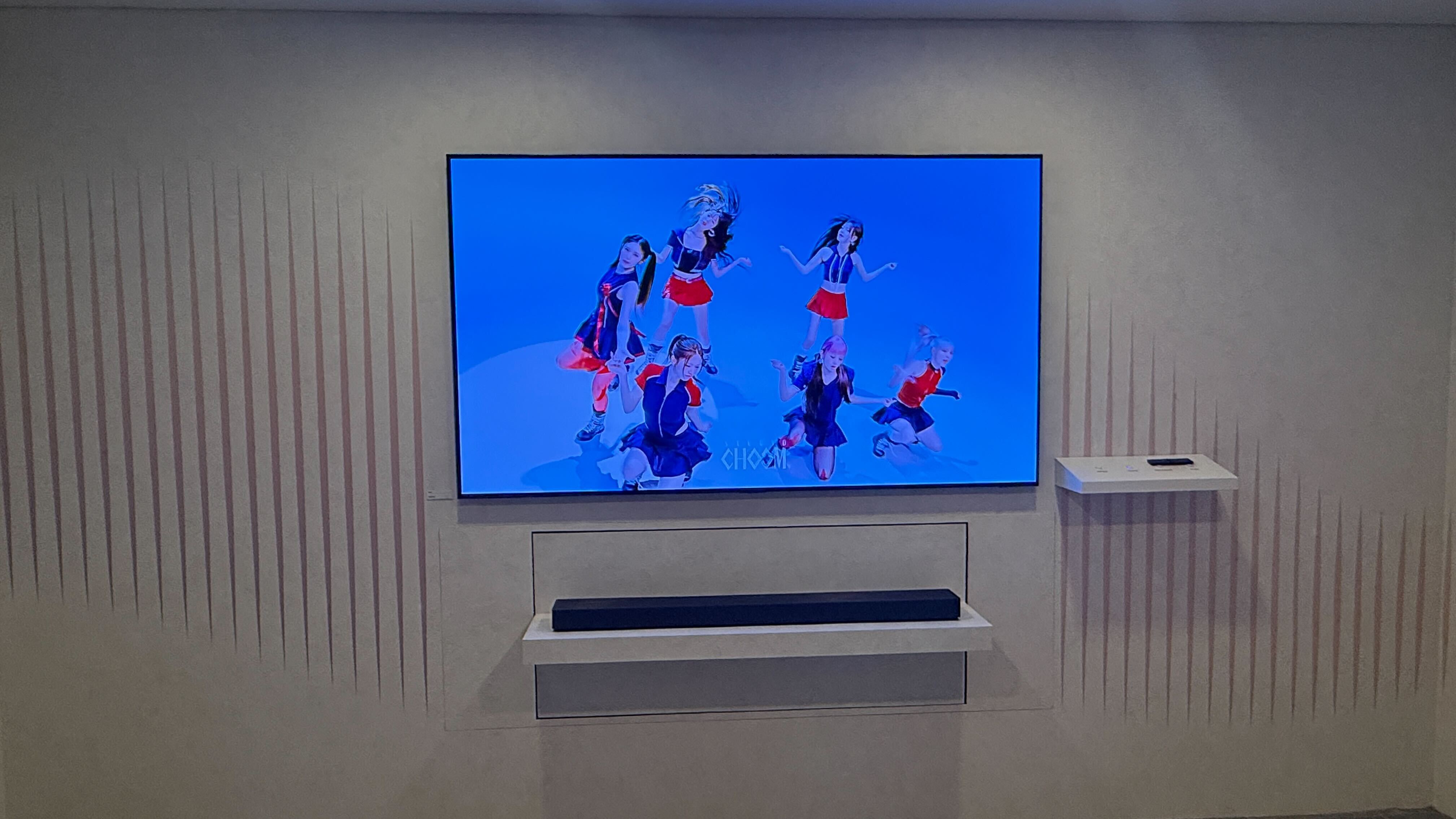 Samsung's HW-QS90H sitting below a wall-mounted TV on a white backdrop
