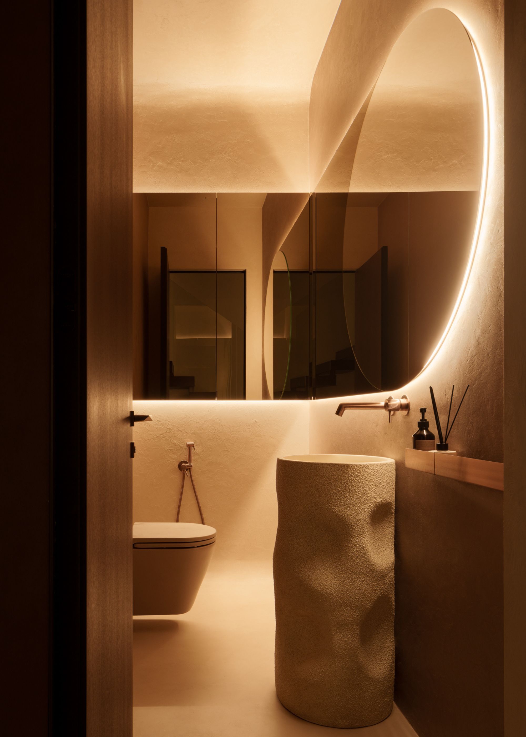 A warm modern bathroom with backlit mirrors and a freestanding microcement basin
