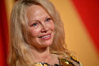 Pamela Anderson wears her hair slightly wavy and her lips glossy as she smiles off camera.