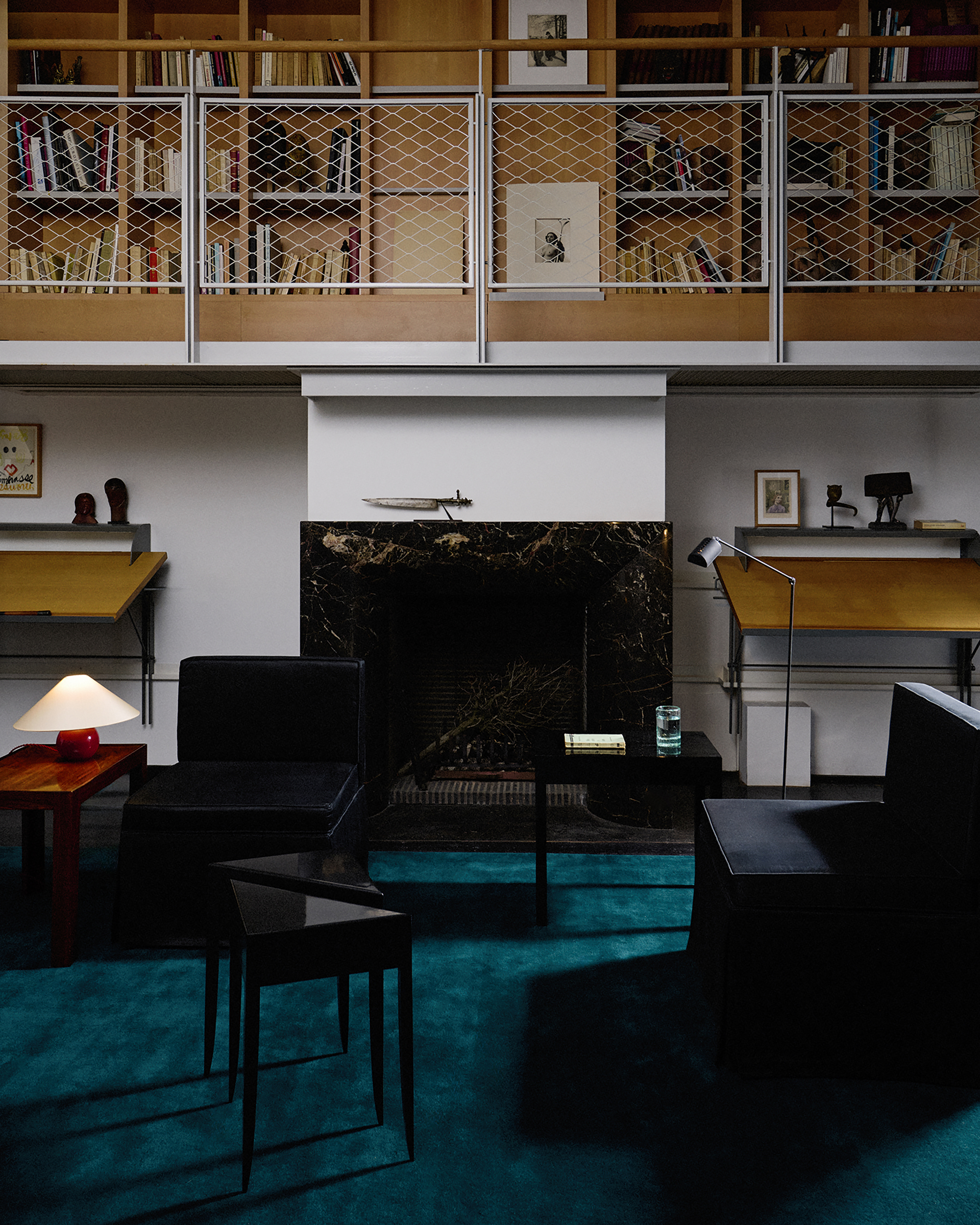 teal colored rug with black marble fireplace surround, black armchairs and a black side table with a book and glass of water on it