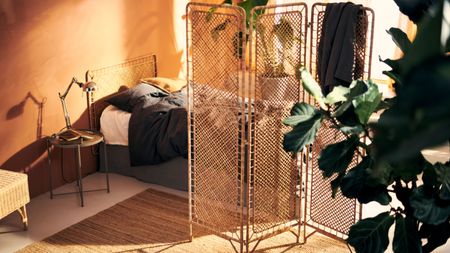 An orange painted bedroom with a low bed with gray sheets and a rattan headboard, there's a rattan room divider separating the space