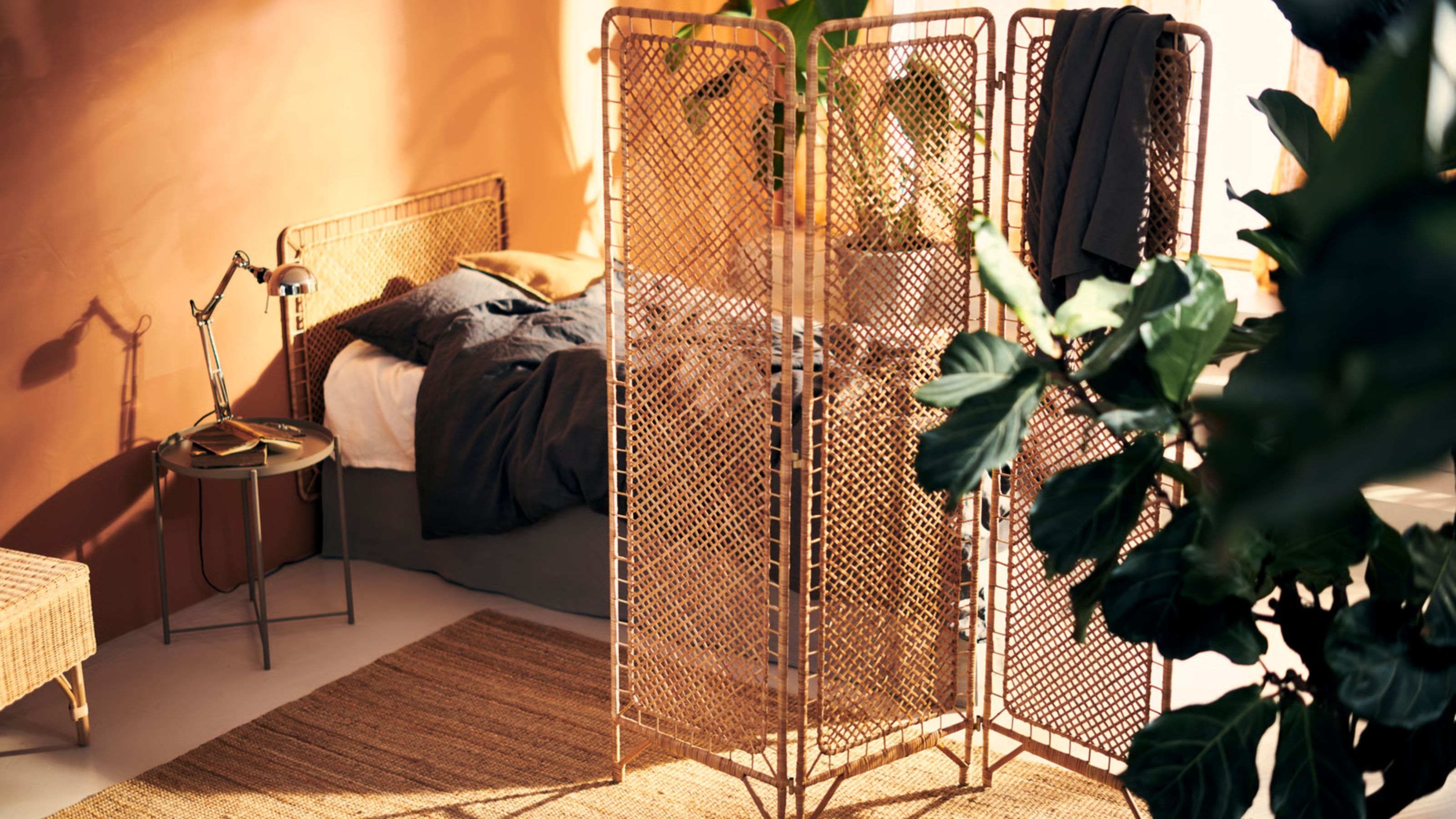 An orange painted bedroom with a low bed with gray sheets and a rattan headboard, there's a rattan room divider separating the space