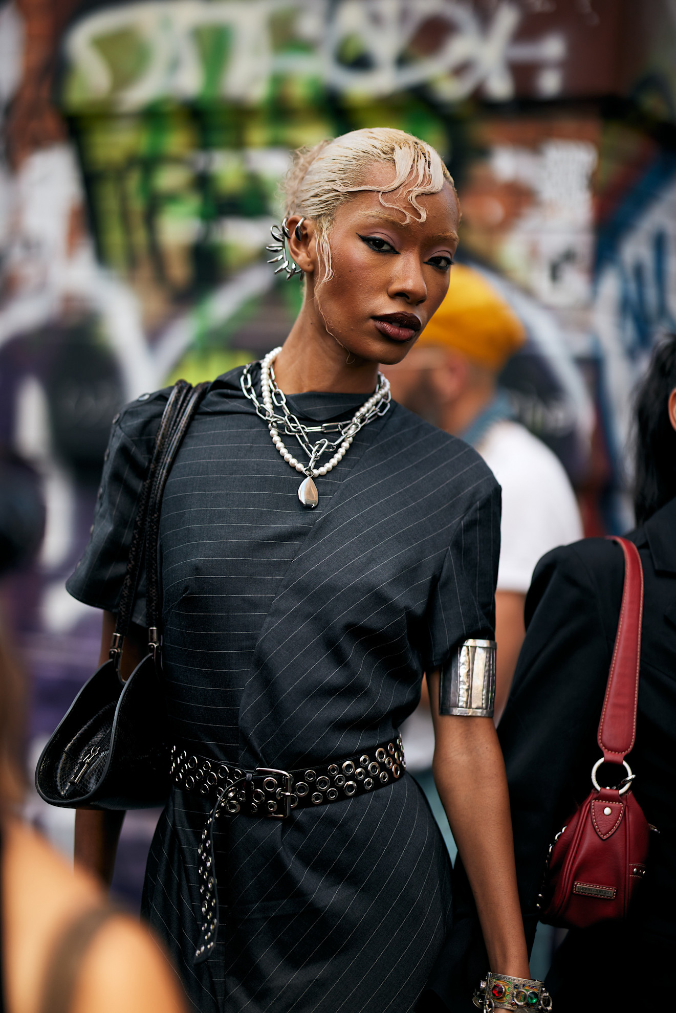 a woman with blonde hair and wavy bangs wearing a black stripe shirt and pearl necklace and silver chain