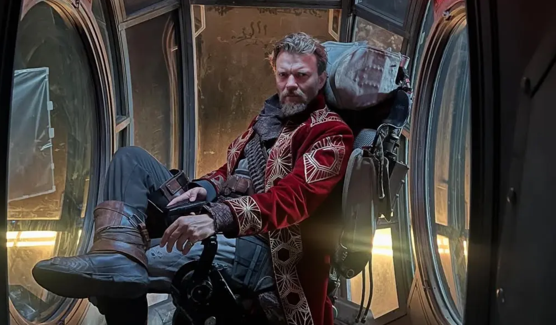 a confident man sits cross-legged in a chair