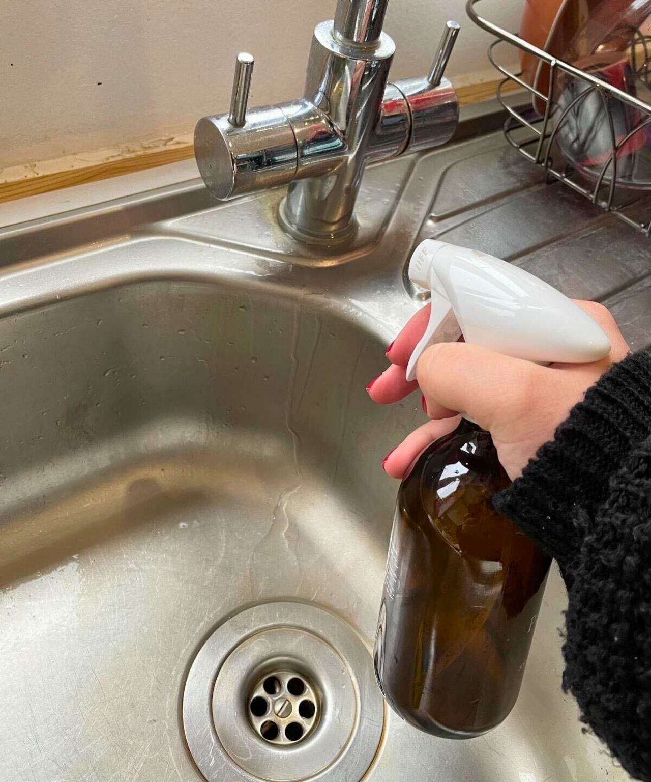 My hand spraying the faucet with my lemon limescale cleaning mixture