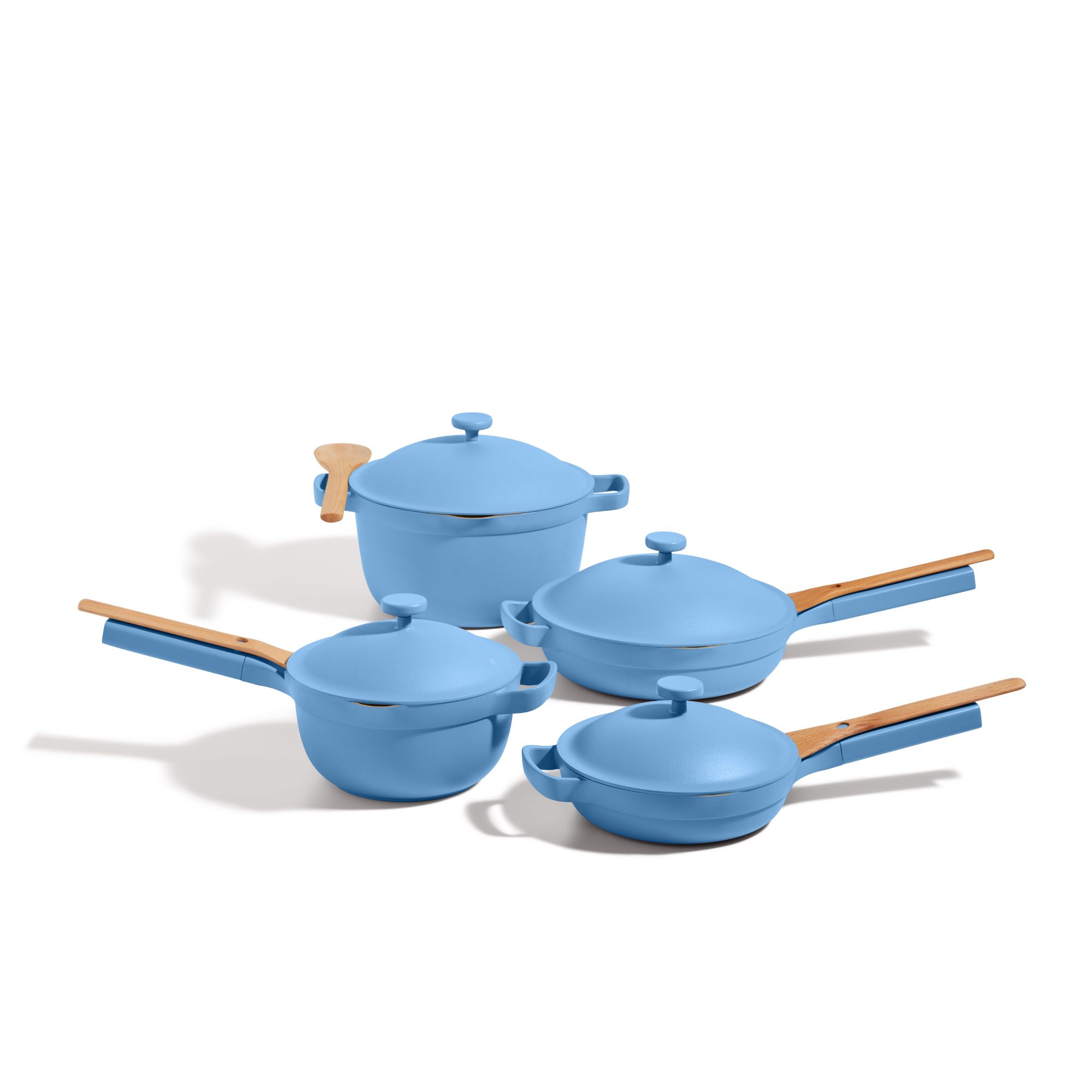 A set of four blue pans, each with matching domed lids and wooden spoons resting on the long pan handles.
