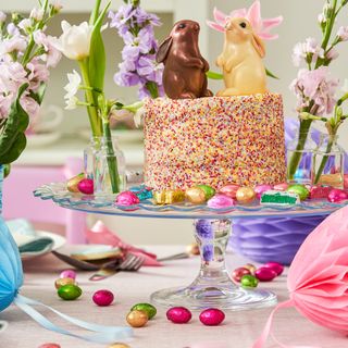 Glass cakestand with colourful cake topped with chocolate bunnies on a bright easter table