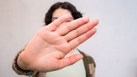 Person holds hand up to camera blocking face.