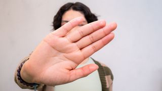 Person holds hand up to camera blocking face.