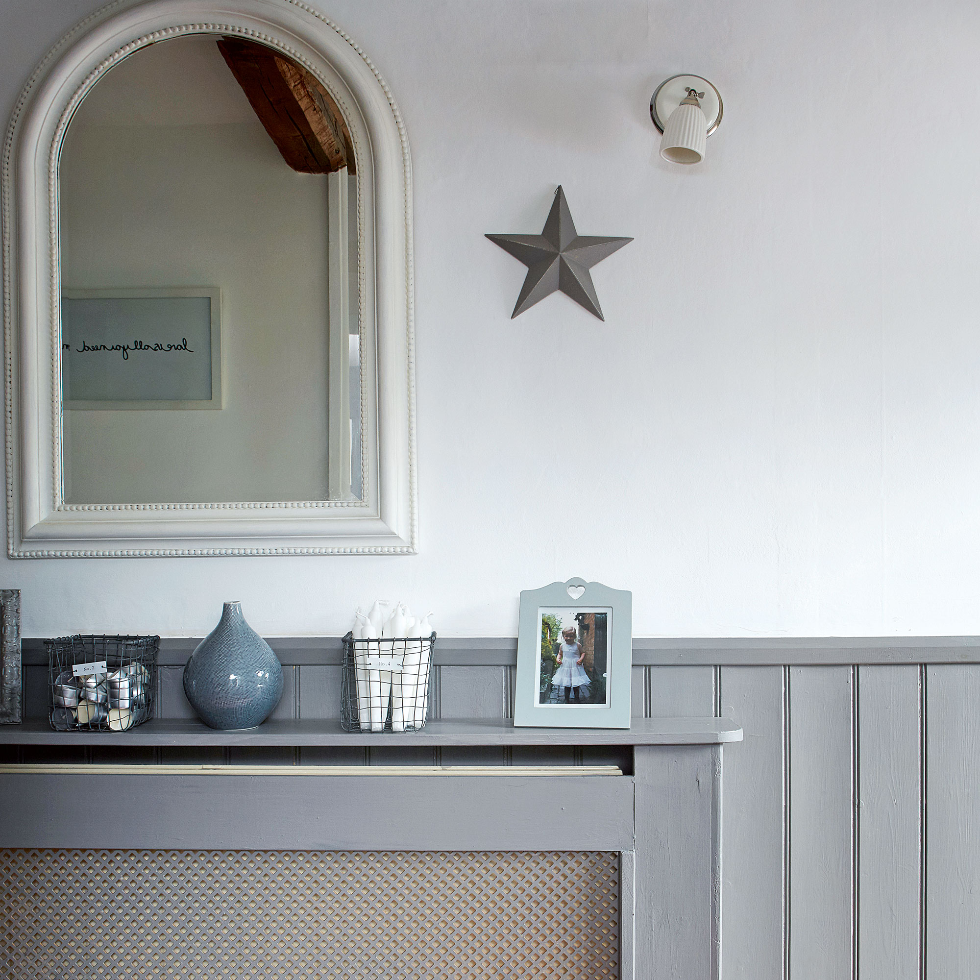 Grey hallway with radiator cover and white mirror over it.