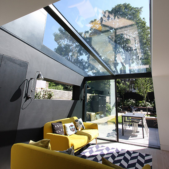 Glass extension with black walls, yellow sofa and black and white Aztec rug