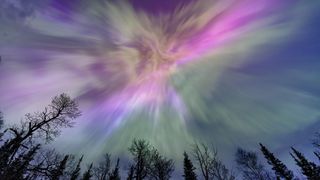 Northern lights erupt over a lake in Minnesota in a dark sky overhead shining rainbow of Aurora light