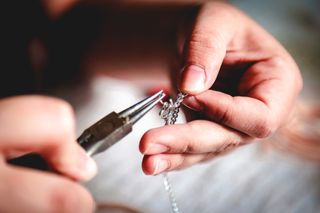 A close up of a pair of hands crafting a silver necklace with a pair of pliers.