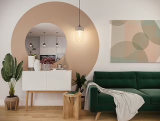 a white wall with a pink circle painted on it, in front of a mirror, a white side table, a green sofa, and plants.