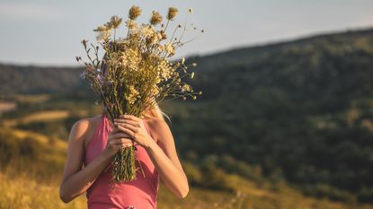 Woman holding a bouquet of dried flowers in front of her face while standing in a meadow