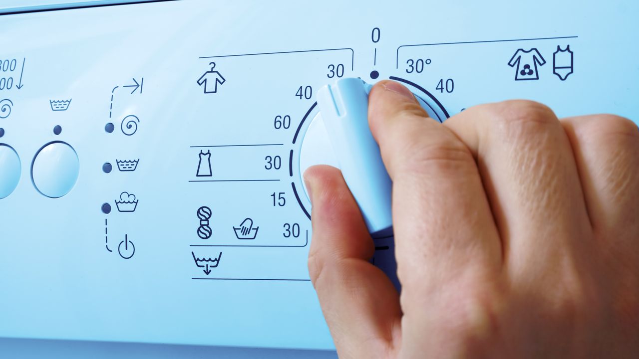 A person operating a white washing machine turning temperature knob to 30 degrees celsius