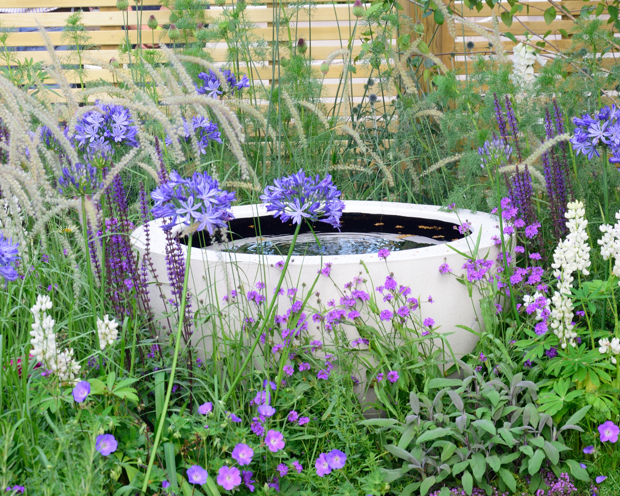 Water feature created using a planter, in a border of blue, white and violet flowers