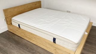 The DreamCloud Luxury Hybrid placed on a light wooden bed frame