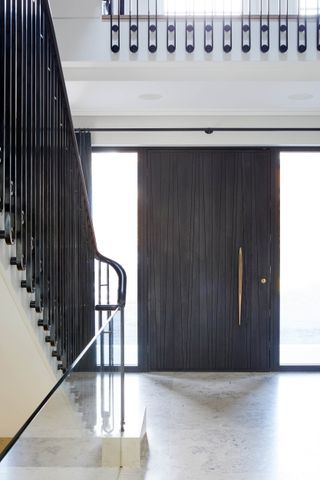 Black wooden front door with gold handle and staircase