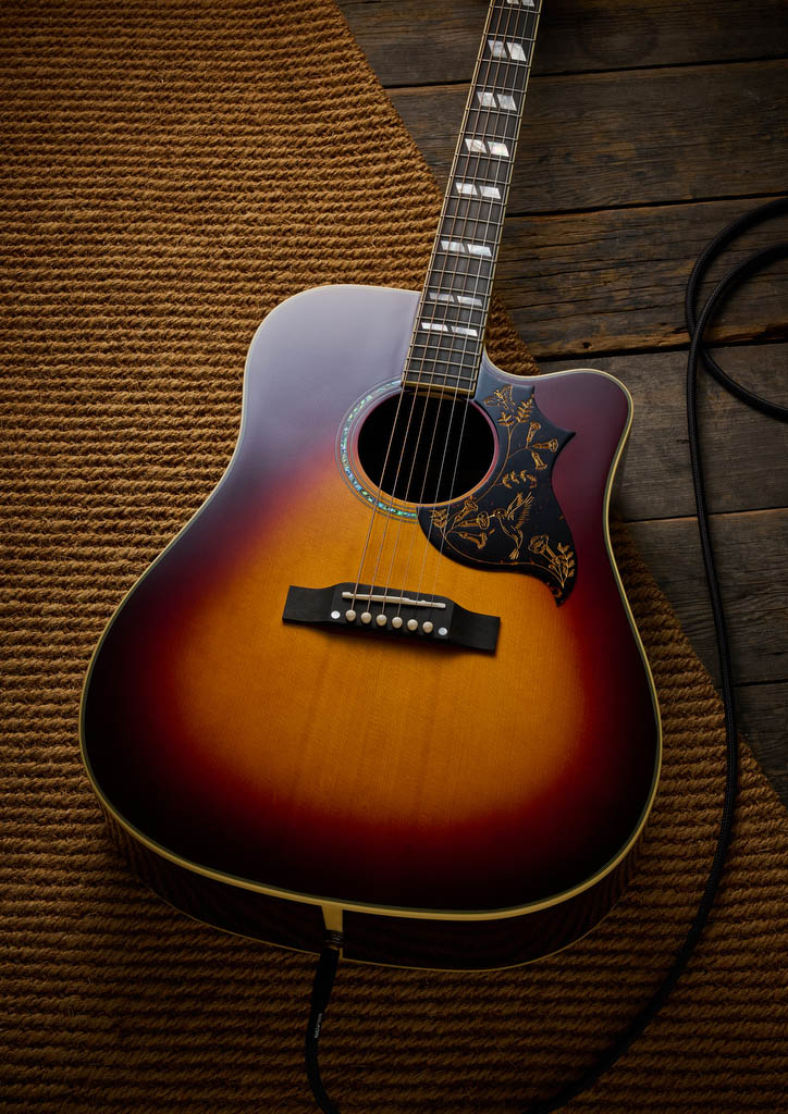The Epiphone Inspired by Gibson Custom Hummingbird photographed in all its glory, in close-up and against a wheat-coloured rug.