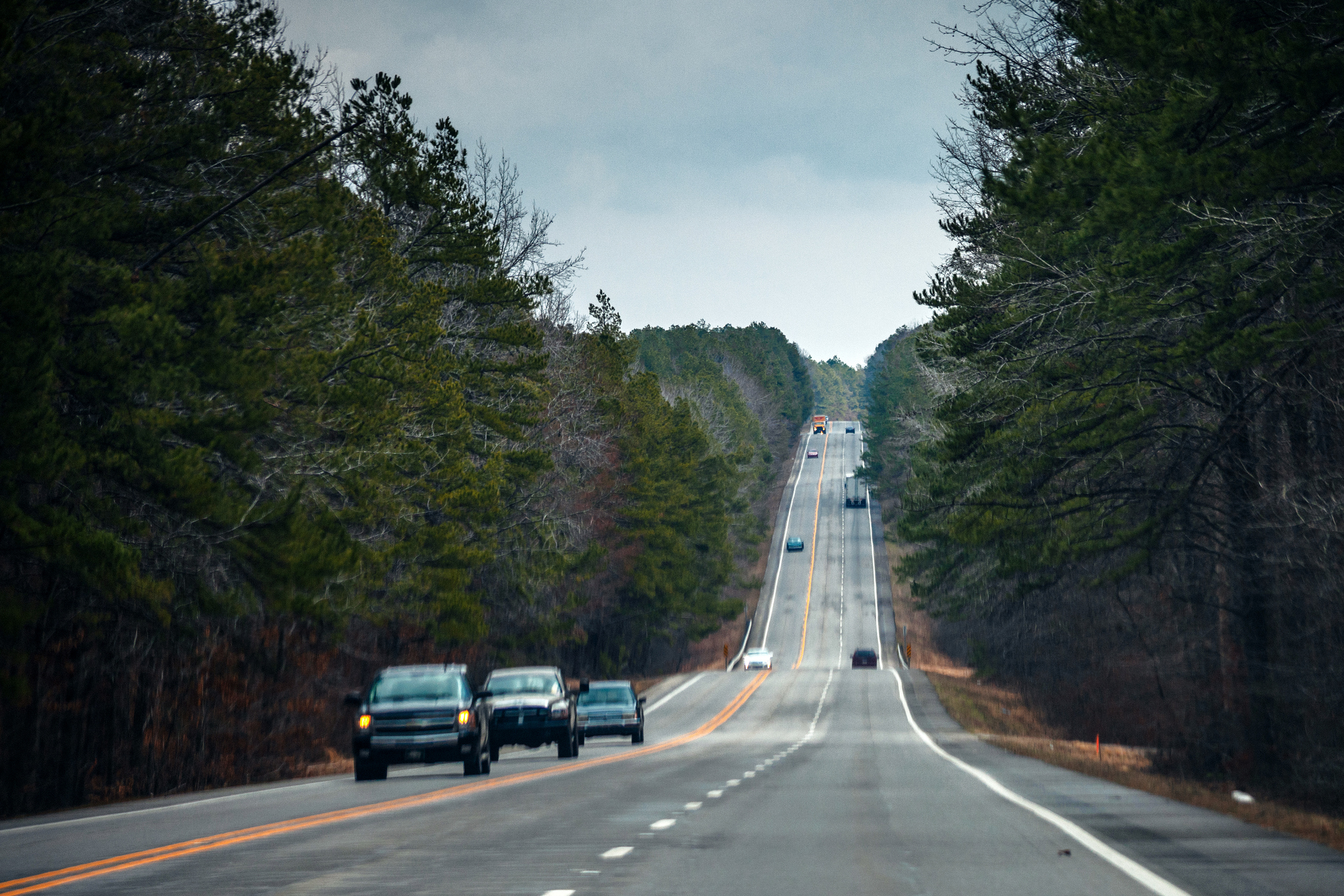 Multiple cars driving down a long highway through a forested area in Arkansas.