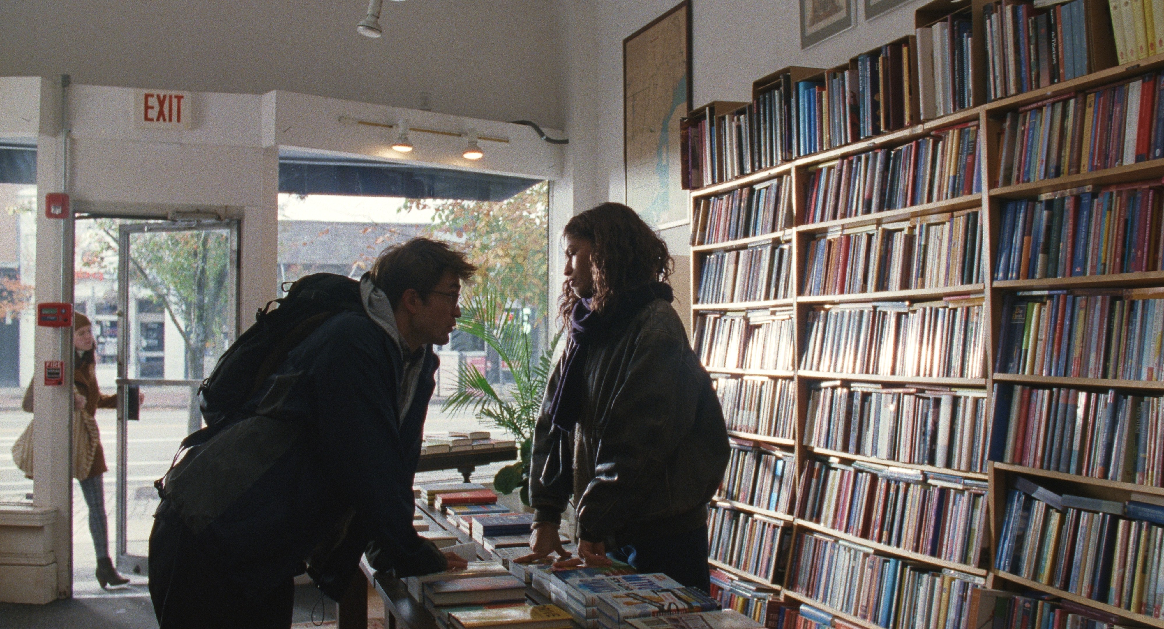 A young couple seen in front of a bookstore's shelving unit stacked with volumes.