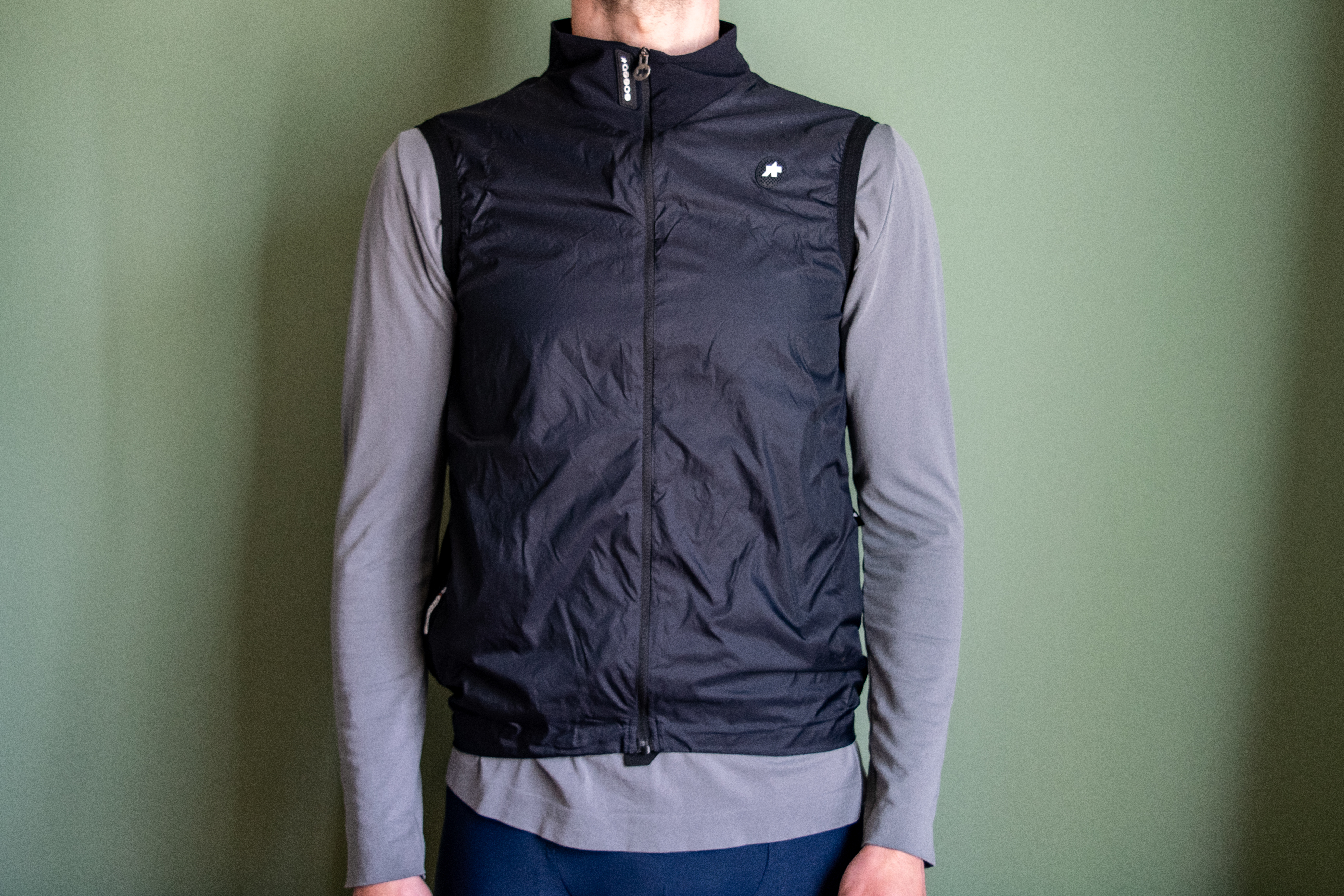 A man wearing a black Assos Tactica gilet over a grey long sleeve shirt