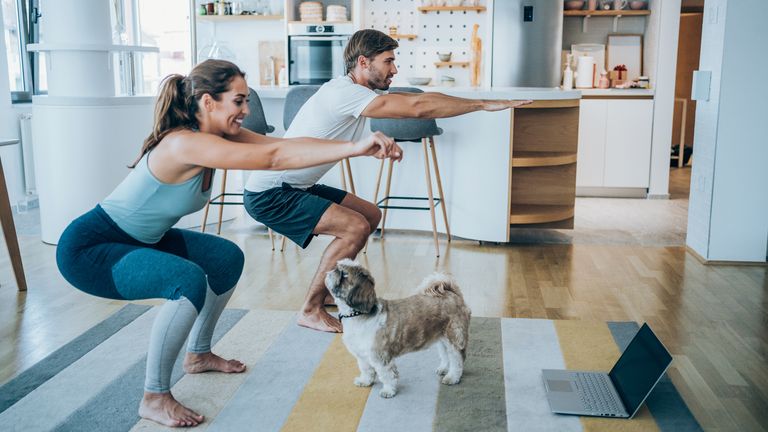 Man and woman complete squats in their home with dog looking at them