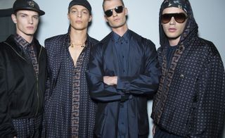 Four male models wearing patterned clothing by Versace in dark shades.
